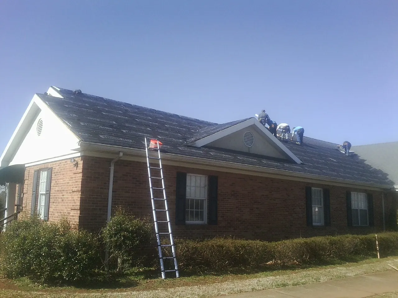 Crew tearing shingles off a brick ranch roof with a ladder set — Metal Roof Repair work by our crew in Eureka